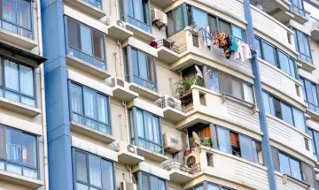 Fasada bloku mieszkalnego z wieloma oknami, balkonami i zamontowanymi klimatyzatorami.